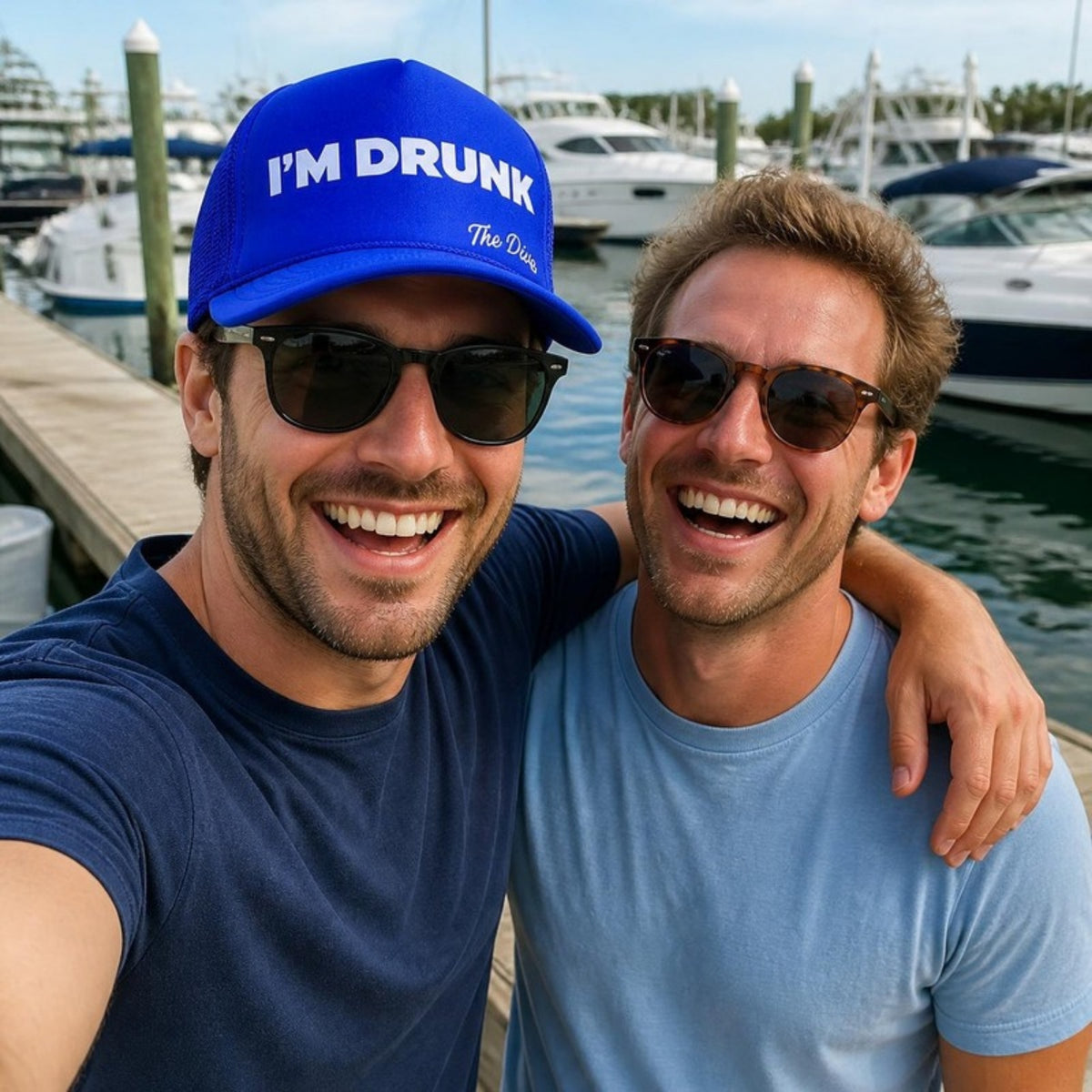 Friends at the marina, one wearing the blue I Am RUNK hat